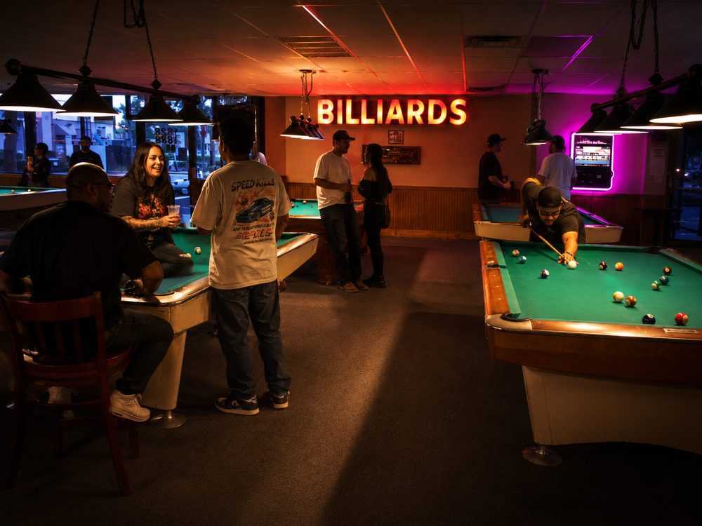 Vibrant group of friends laughing, socializing and drinking around a pool table