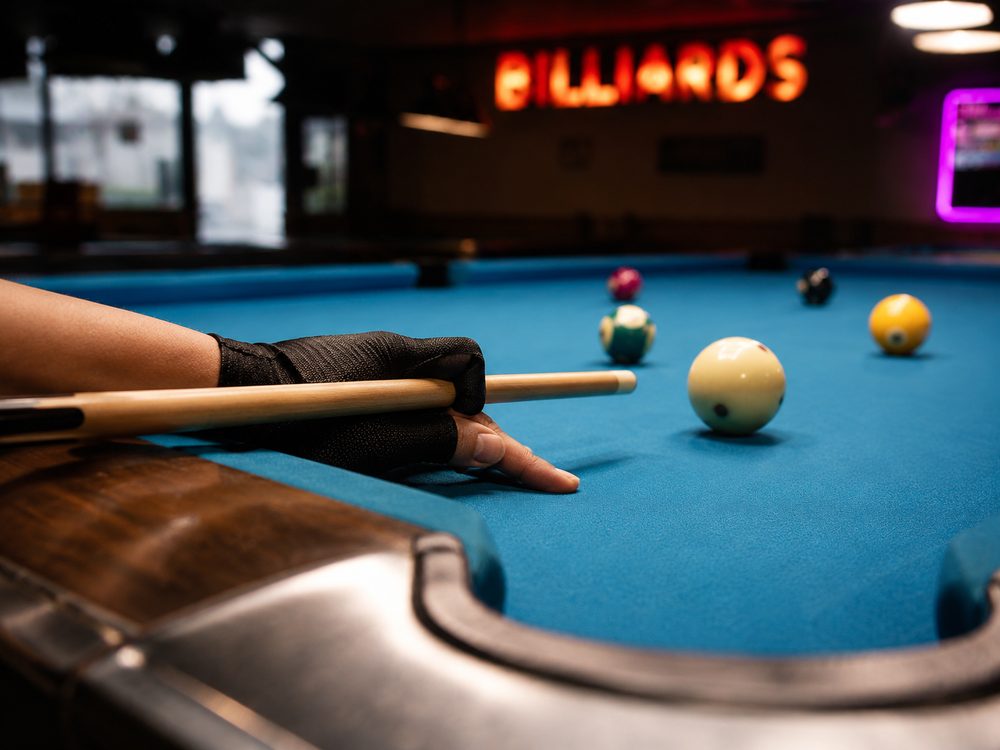 Macro close-up shot of player in black glove aiming cue at cue ball on a pool table